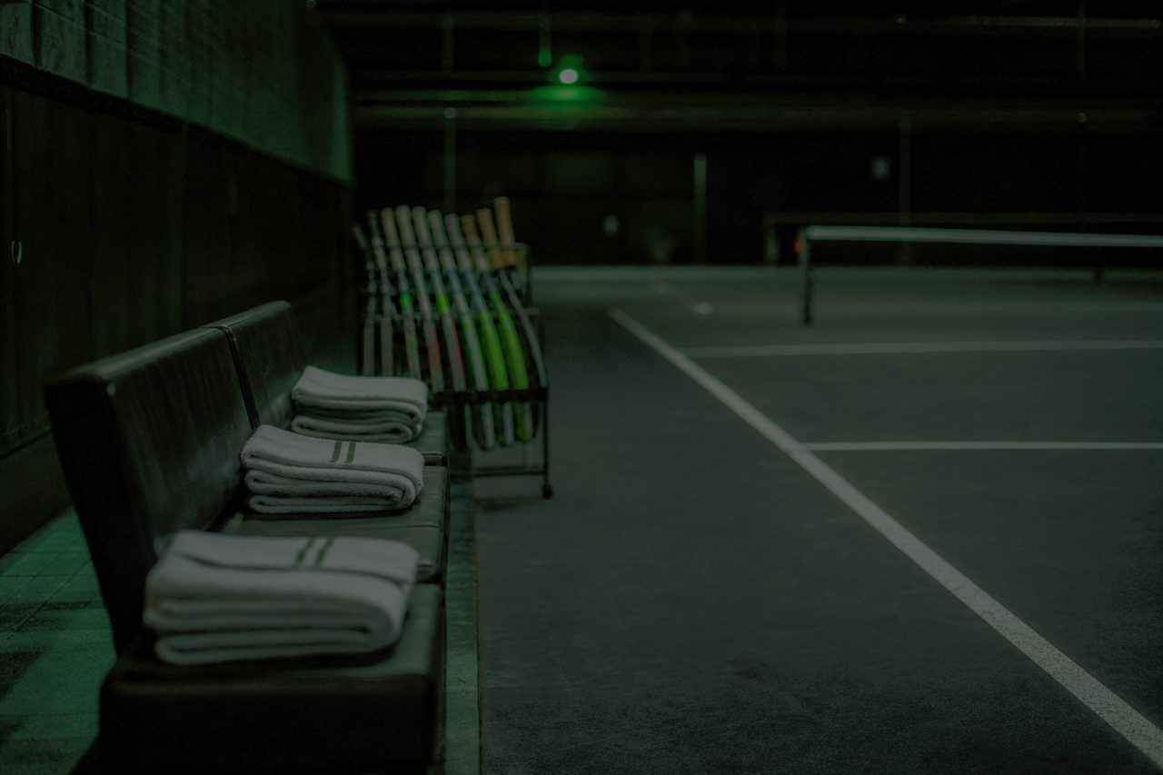 Leere Spielerbank mit Handtüchern und Schlägerständer an einem Hallenplatz