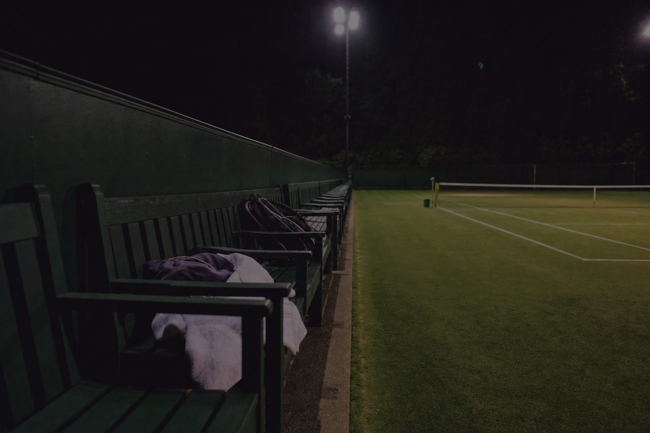 Leere Spielerbank mit Handtüchern und Schlägertasche an einem Rasenplatz bei Nacht