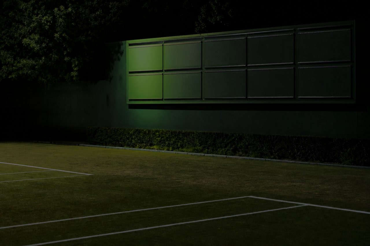 Wand mit leeren Ergebnistafeln neben einem Tennisplatz bei Nacht