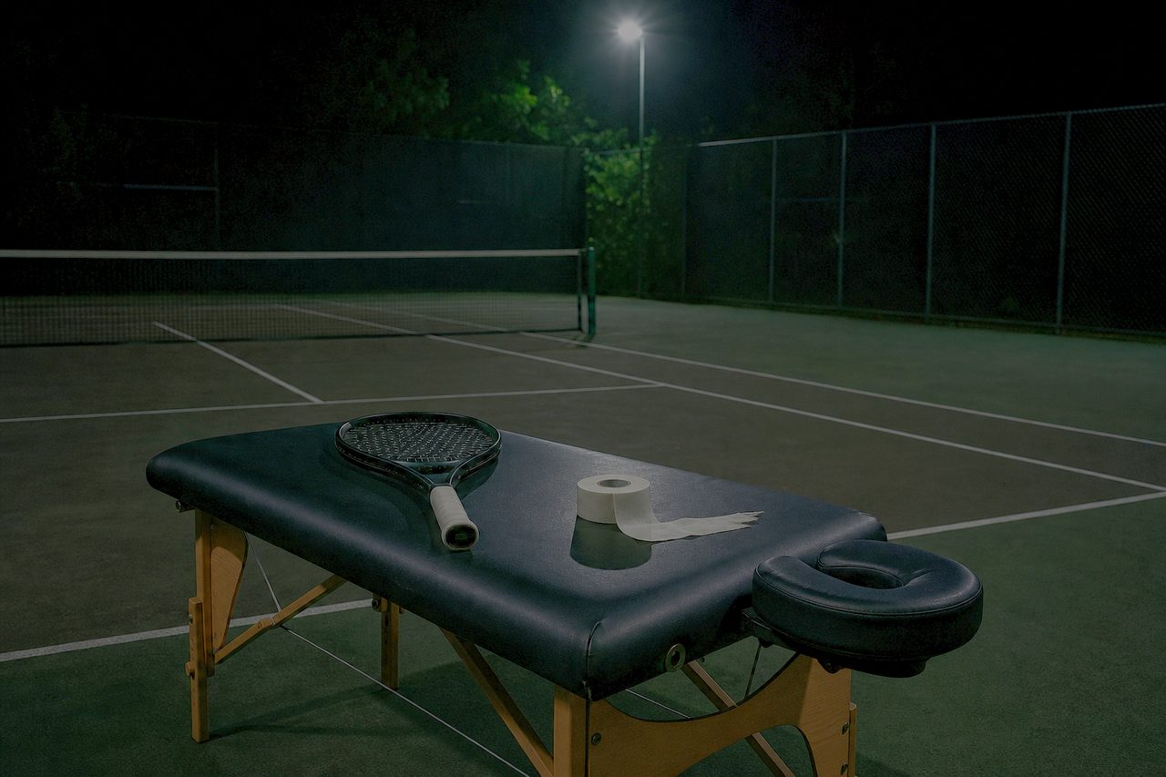 Behandlungsbank neben einem dunklen Tennisplatz mit Tapeverband und Schläger
